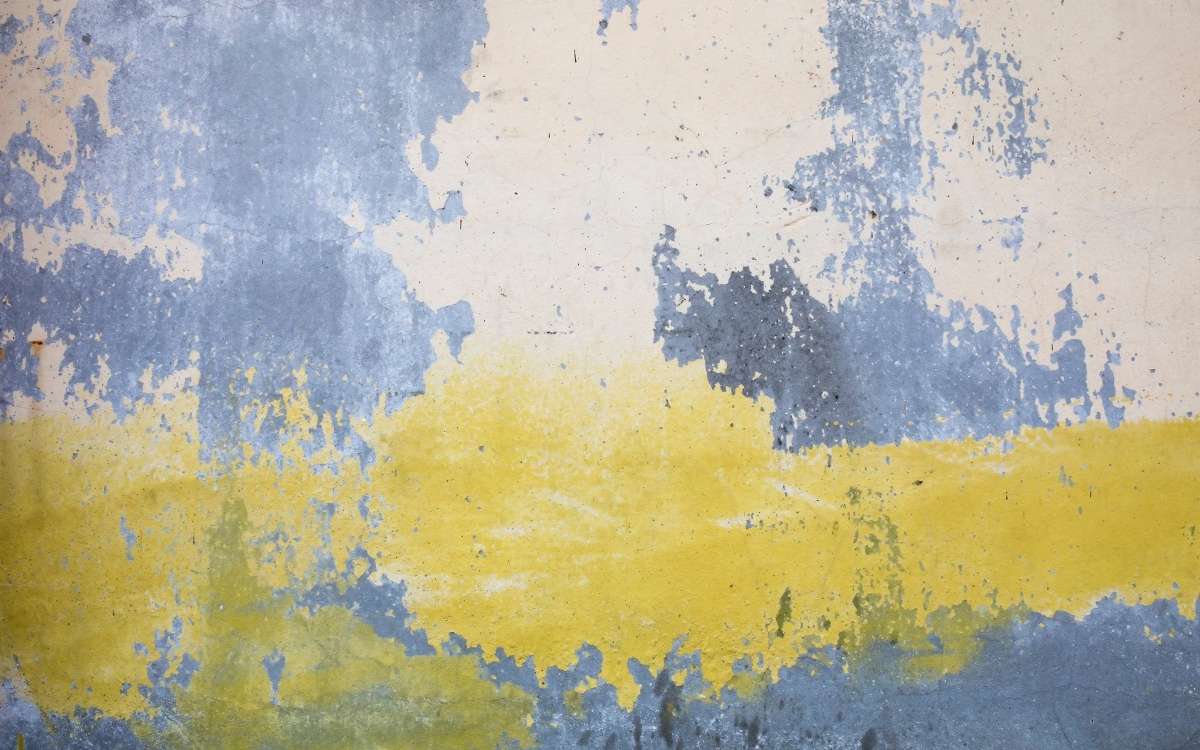 A concrete wall with uneven yellow and peach colored paint