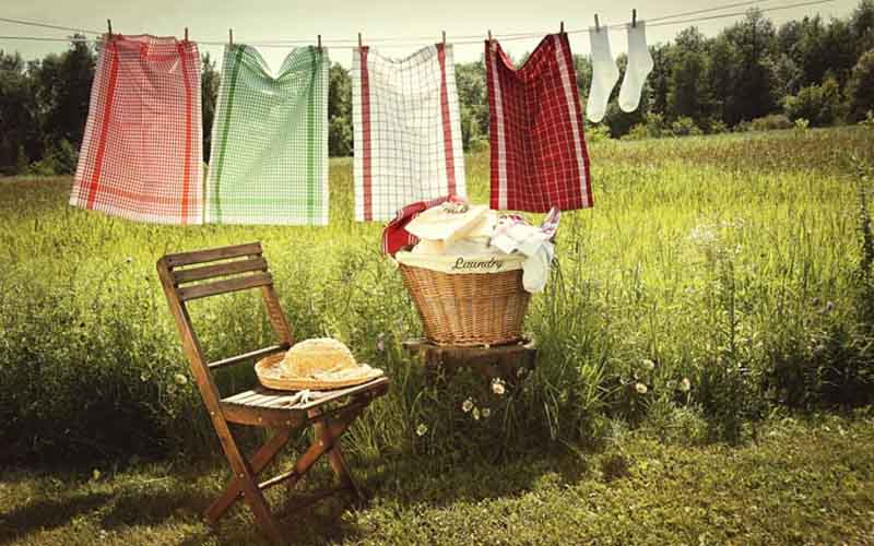 red and white sheets hanged on clothes line to dry with grasses underneath, a chair and a basket nearby