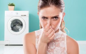 Photo of a woman pinching her nose in a loundry room with washing machine behind her