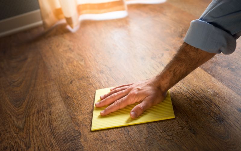 Photo of a hand with a rag cleaning the wood floor