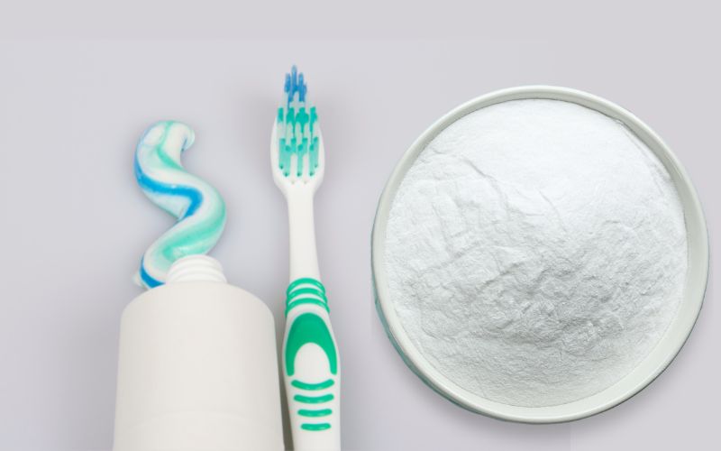 A tube of toothpaste and a toothbrush beside a bowl of white powder 