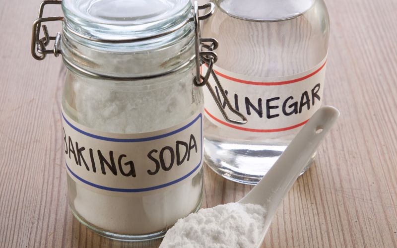 Photo of a jar of baking soda, a botle of vinegar and a spood with white powder