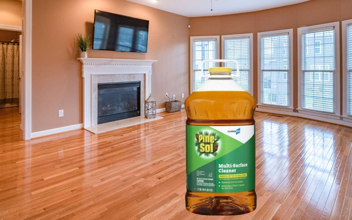 A bottle of Pine-sol on hardwood floors with large windows and fireplace at background