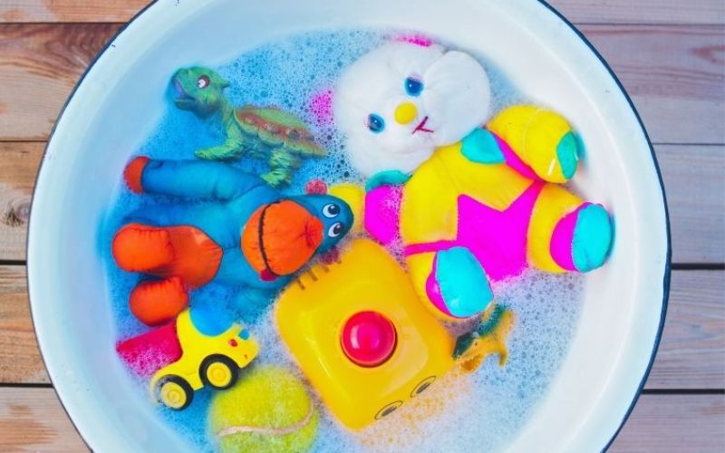 Colorful toys soak in soap and water in a white basin 