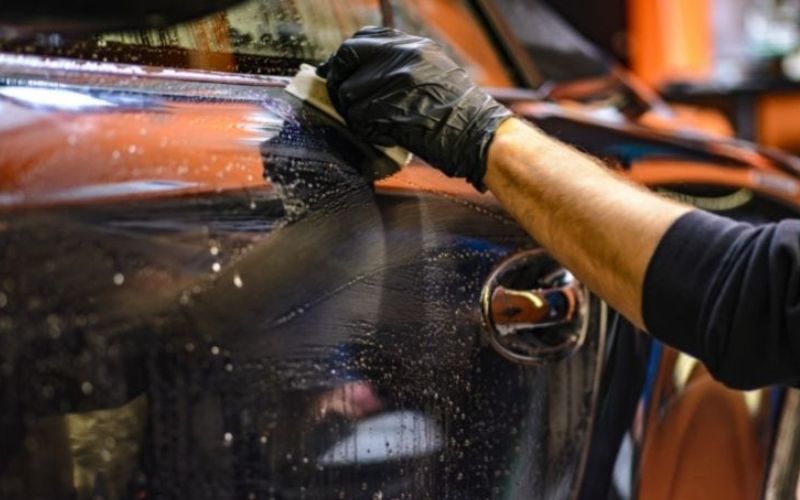 A hand with black glove uses a sponge in cleaning the car.