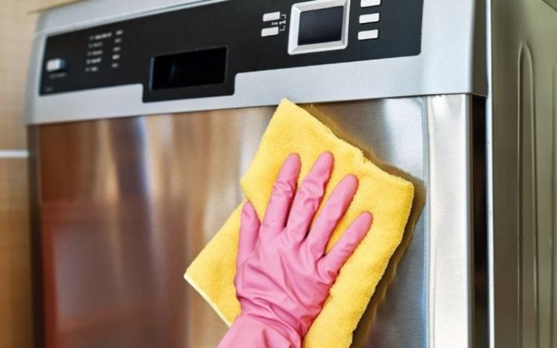 A hand with pink gloves uses a yellow rug for cleaning a dishwasher
