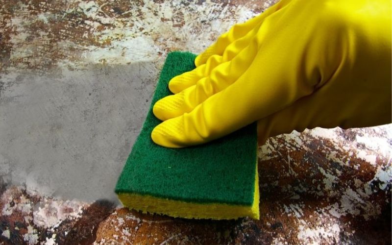 A hand with yellow gloves uses a sponge for cleaning dirty pots and pans