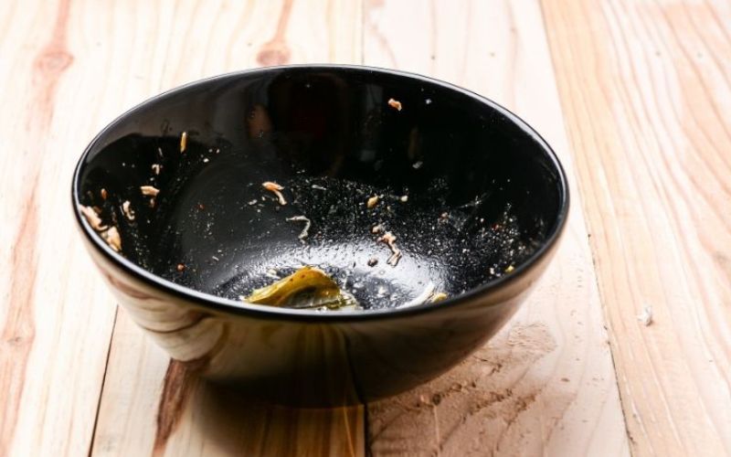 A black dirty bowl on a wooden top that needs cleaning