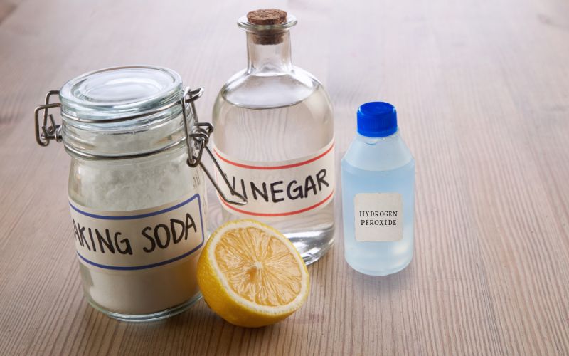 Image showing a jar of baking soda, a bottle of vinegar, a slice of lemon, and a small bottle og hydrogen peroxide on a wooden top