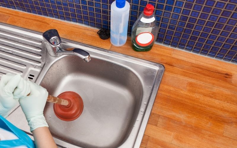 Phot of a pair of hands holding a plunger working on a sink