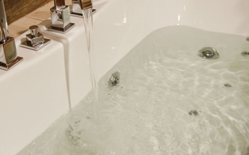 Image of a water filled bathtubs with running water from faucet