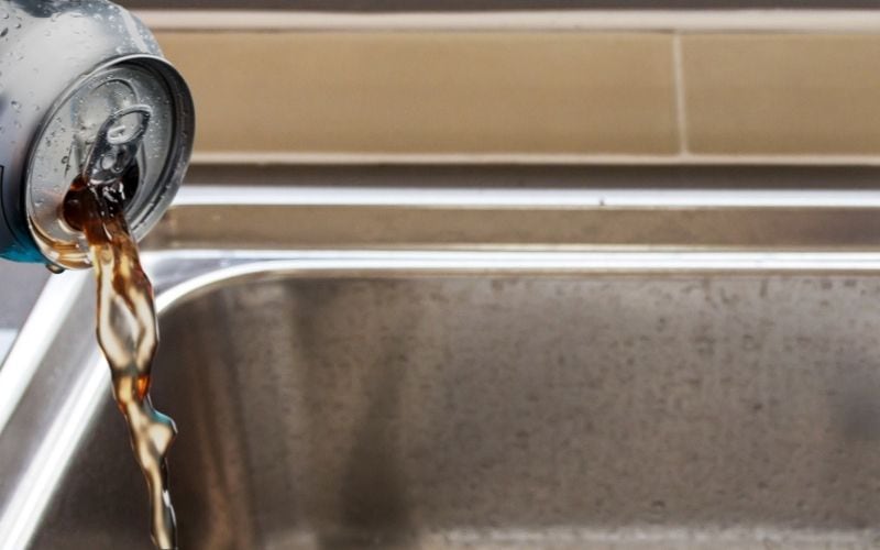 Image of a can of cola being poured over the sink