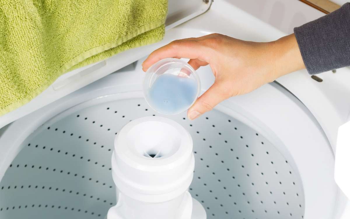 female hand pouring dish soap liquid into washing machine
