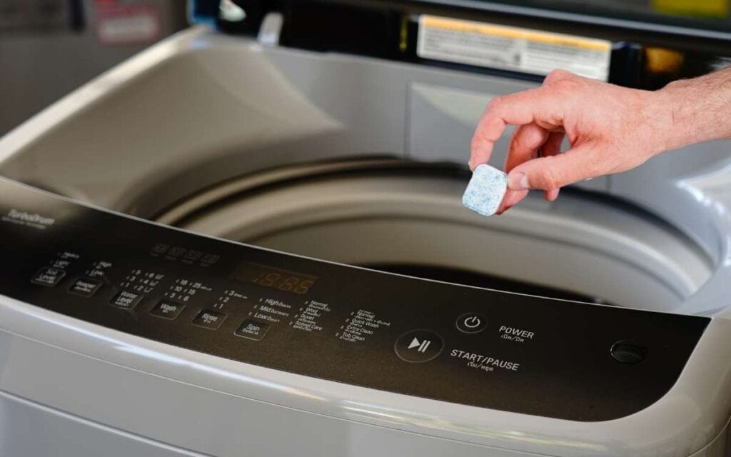 Hand of a man holding dishwasher cleaner over a washing machine