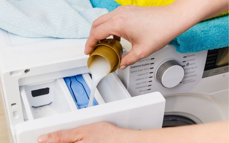 image of a hand pouring liquid detergent into washing machine with the laundry