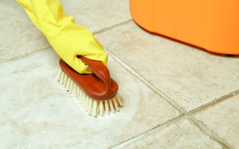 photo of a gloved hand holding a brush while cleaning the floor tiles