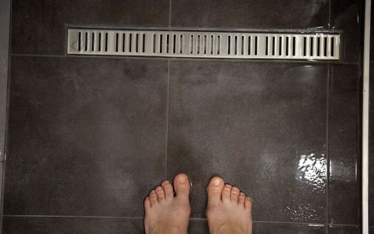 Image of feet on the bathroom floor near the drain where drain worms could live