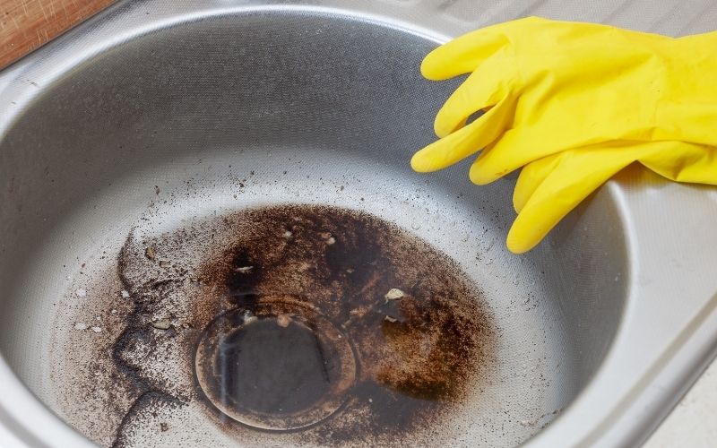 Photo of a clogged sink with water and dirt and a pair of yellow gloves