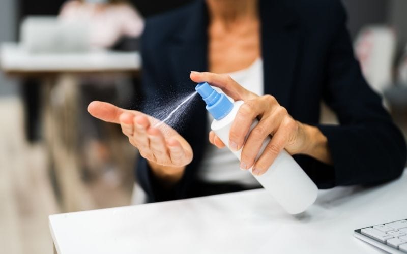 Photo of two hands of a woman holding spray bottle spraying liquid on her other hand