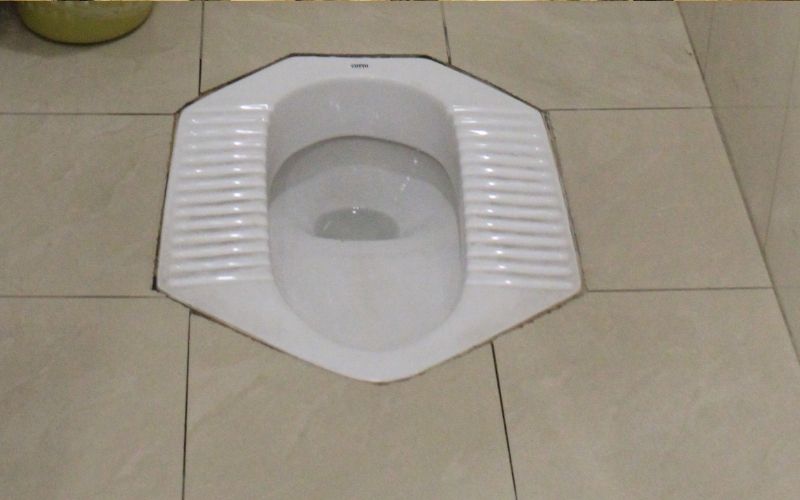 Photo of a white squating toilet with light brown floor tiles