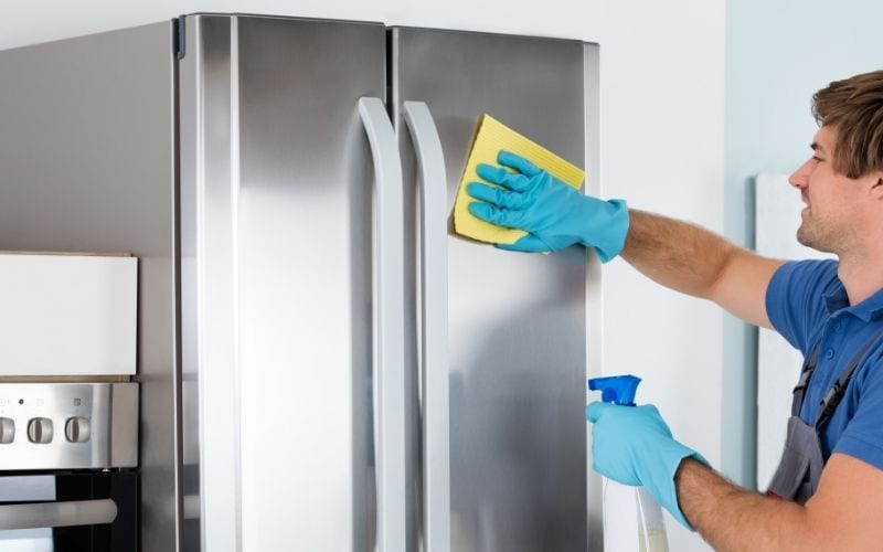 Picture showing a pair of hands cleaning a refrigerator with a rag while spraying the surface