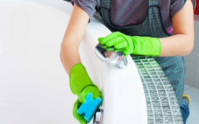 A person with gloved hands while cleaning a bathtub with the use of sponge