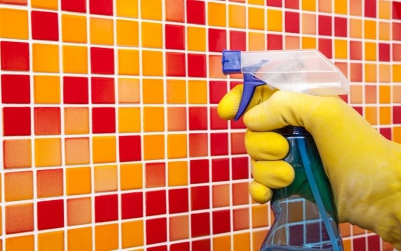 Photo of a hand holding a spray in front of tiled wall