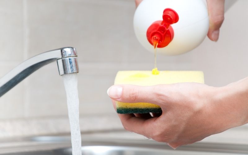 Image showing a pair of hands holding a white container, a sponge beside a running water from faucet 