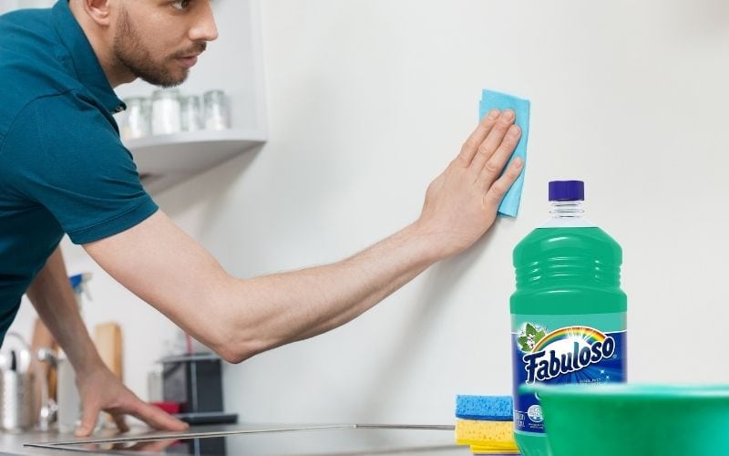 Photo of a man cleaning the wall above a counter top with cleaning materials beside him