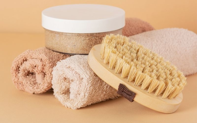 Photo of two rolled towels, a small jar of scrub and a brush