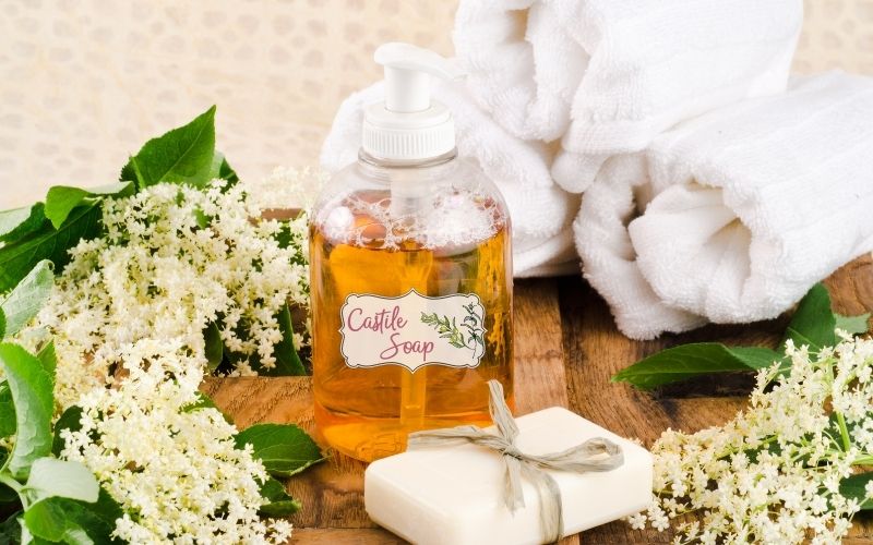 Photo of a of bunch flowers, some towels a bar soap and a bottle of castile soap in the middle