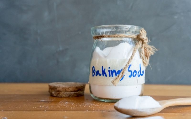 Photo of baking soda in a jar and spoon on a wooden table top that can be used as body wash
