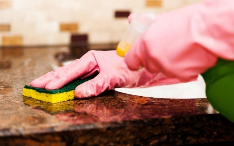 Photo of a gloved hand with sponge cleaning the wooden surface