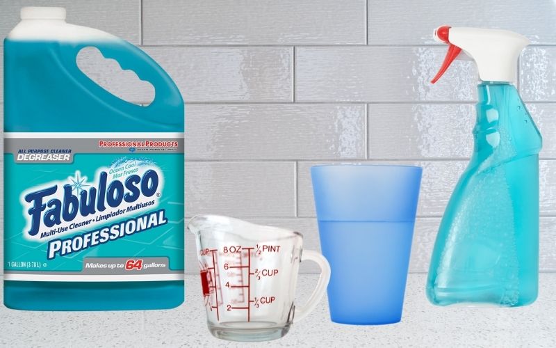 Image of a gallon of fabuloso a measuring cup a glass of water and a spray bottle with blue liquid