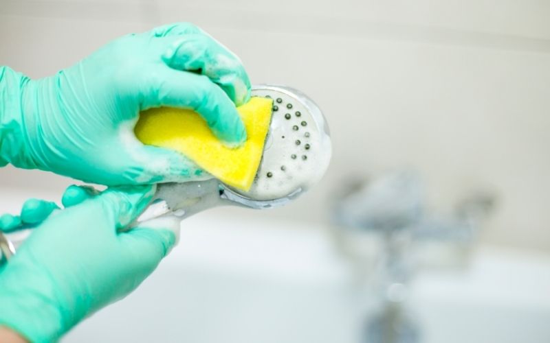 Phot of a pair of hands cleaning a shower head with sponge