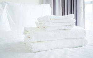 Folded white towels from hotelon a bed with white sheets