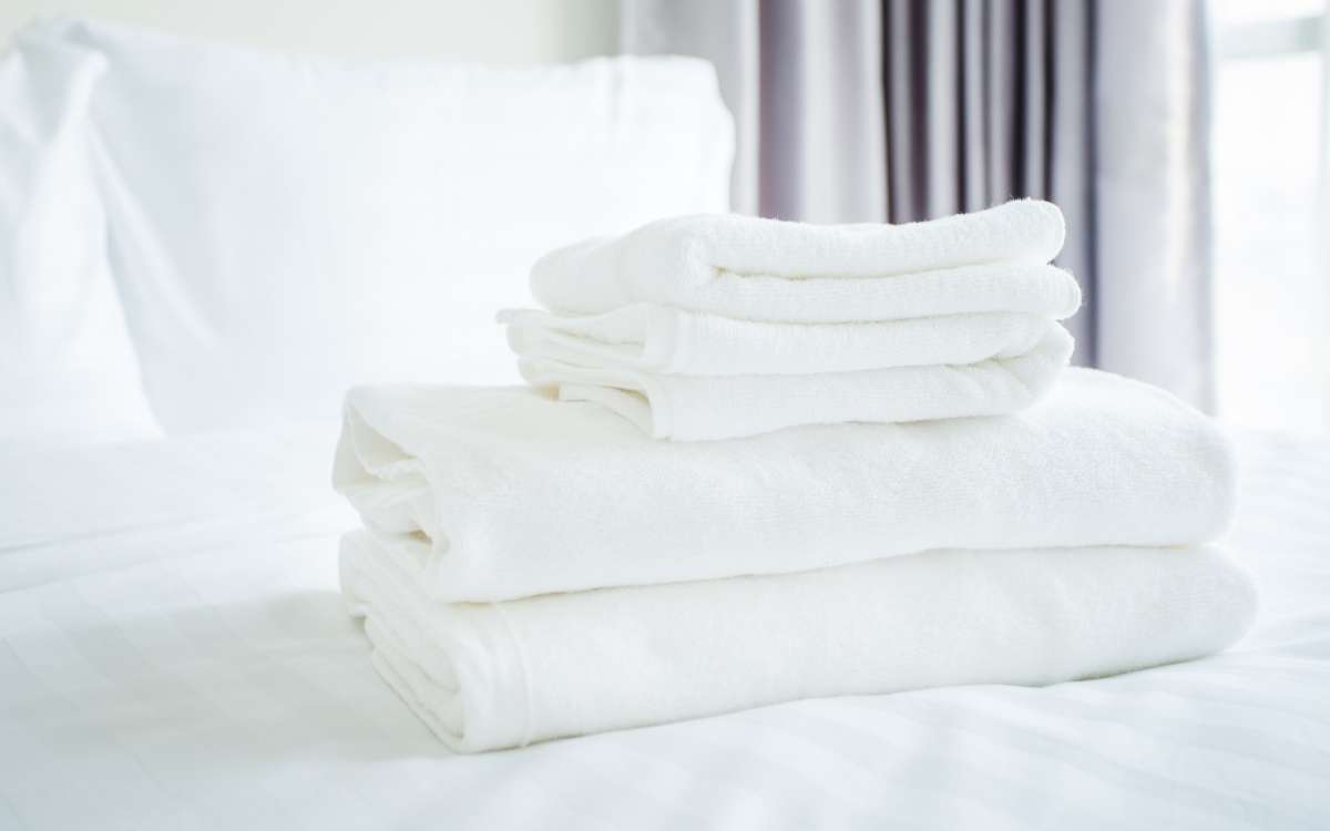 Folded white towels on a bed with white sheets
