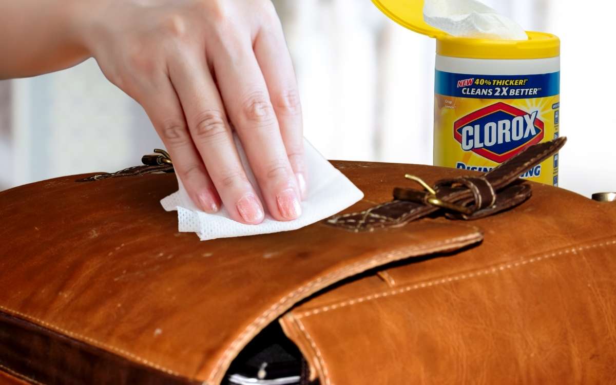 A hand with wipes on a leather bag with Clorox wipes on background_Can You Use Clorox Wipes on Leather